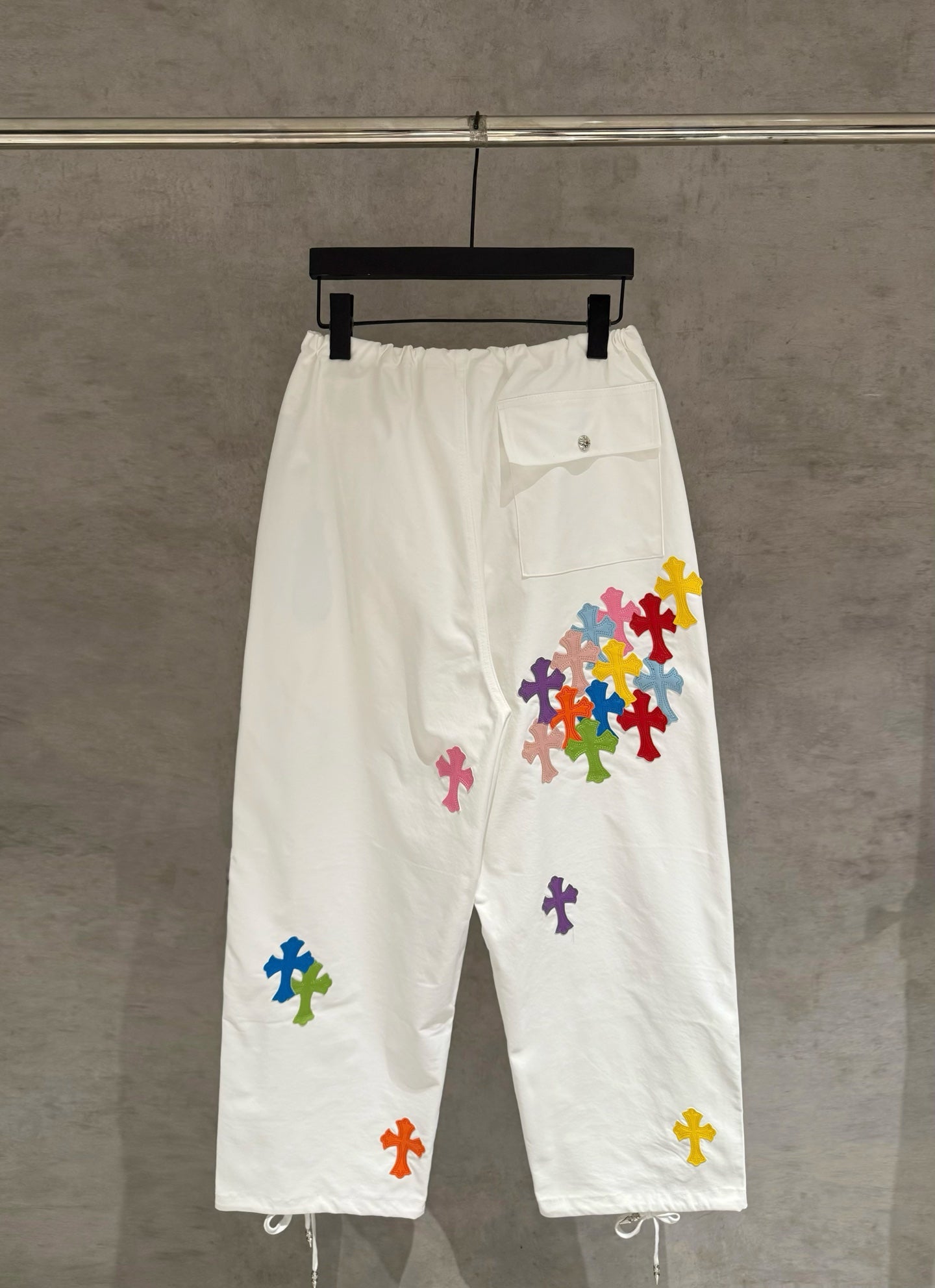 White cargo pants with elastic waist, drawstring, and multicolor cross appliques