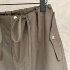 Olive cargo pants close-up with drawcord tie, side flap pocket, and snap-button detail