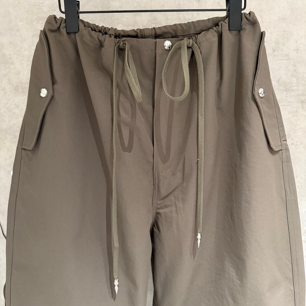 Olive cargo pants close-up: elastic waistband with drawcord, front seam, and snap-button tabs