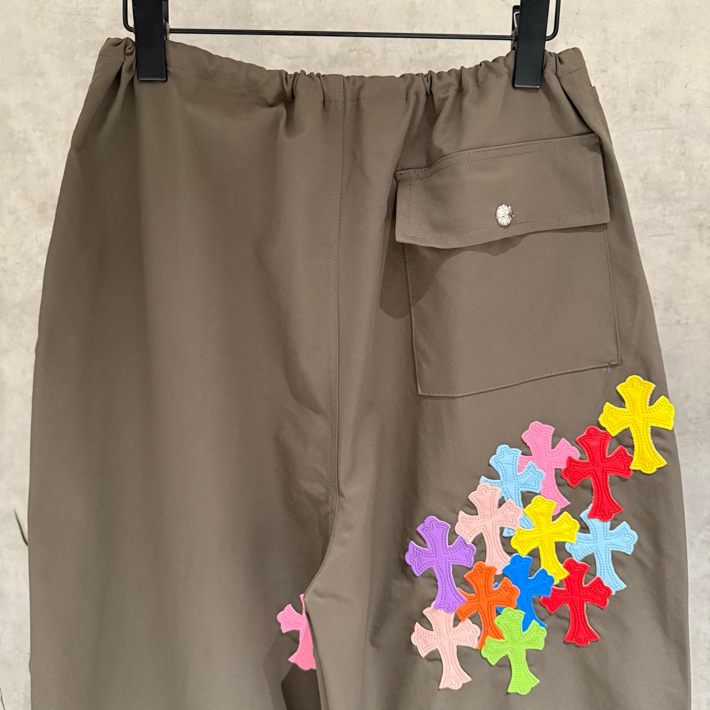 Olive cargo pants back view with elastic waistband, snap pocket, and colorful cross patches