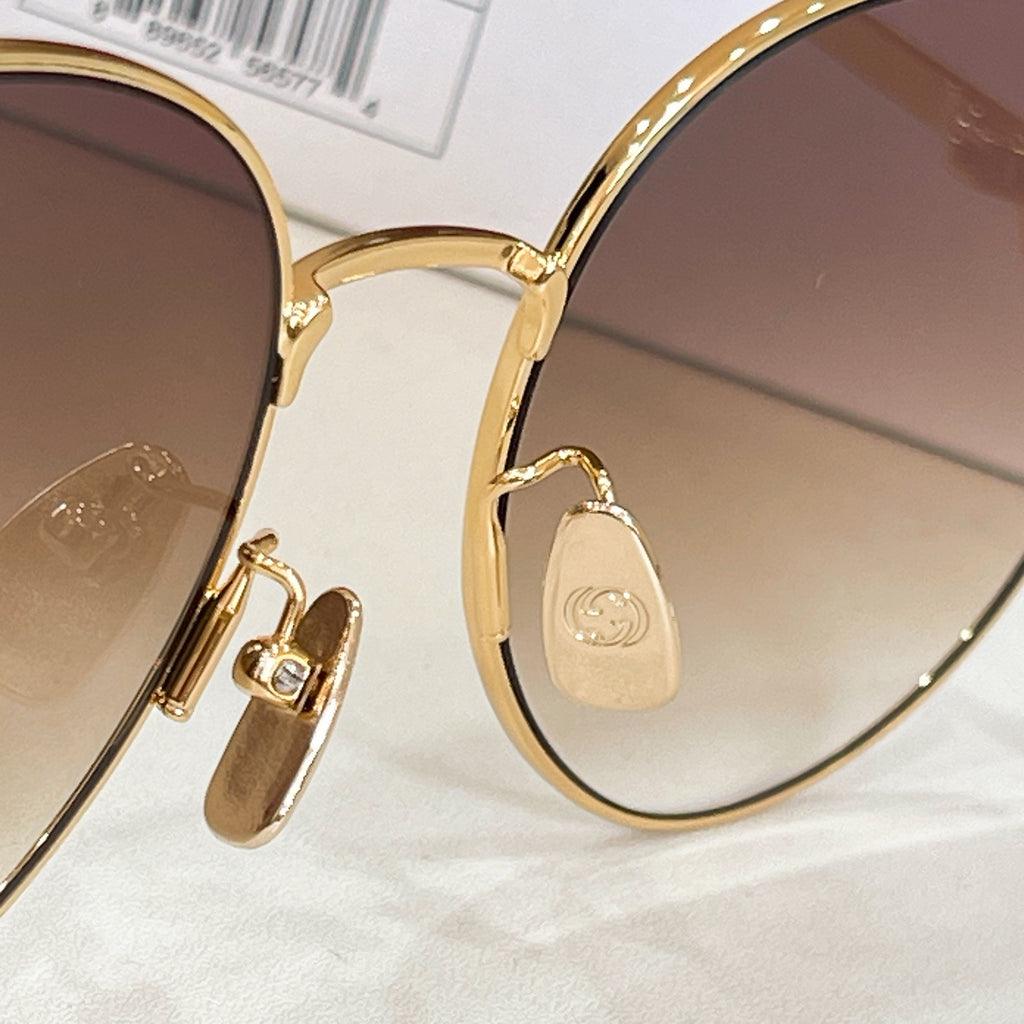 Gold-tone sunglasses detail: engraved temple plate with logo, round lens edge.