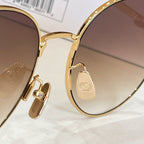 Gold-tone sunglasses detail: engraved temple plate with logo, round lens edge.