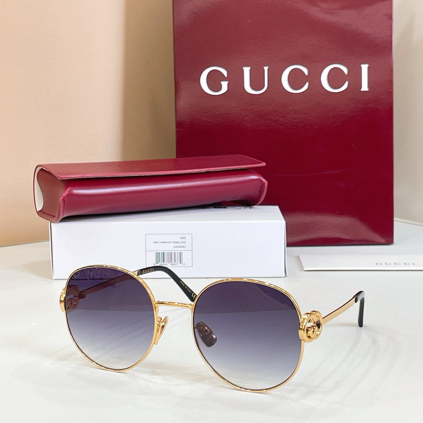 Round sunglasses with gold-tone frame and dark blue tinted lenses, black metal arms.