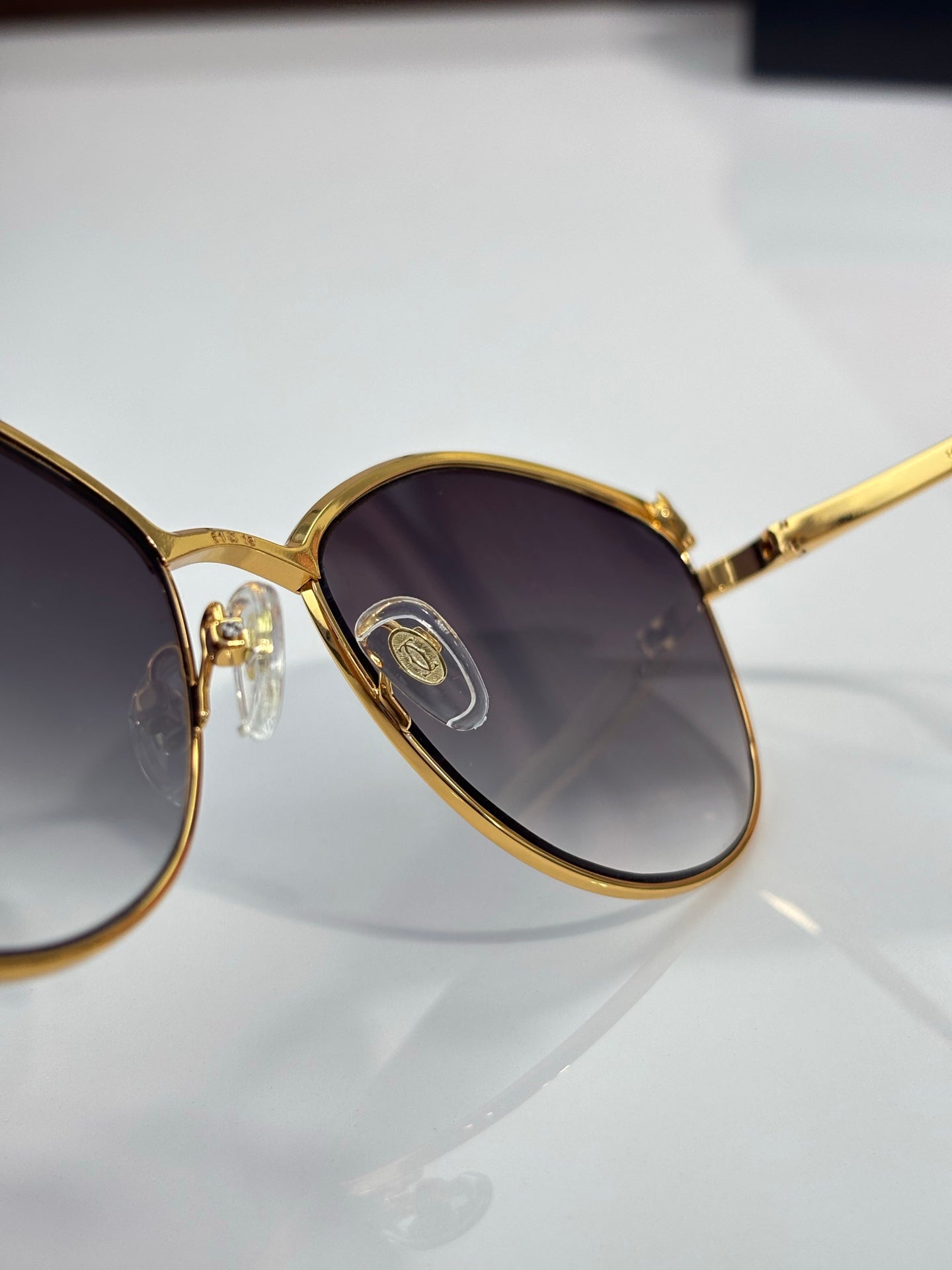 Close-up of gold round sunglasses frame with dark tinted lenses and gold temple detail.