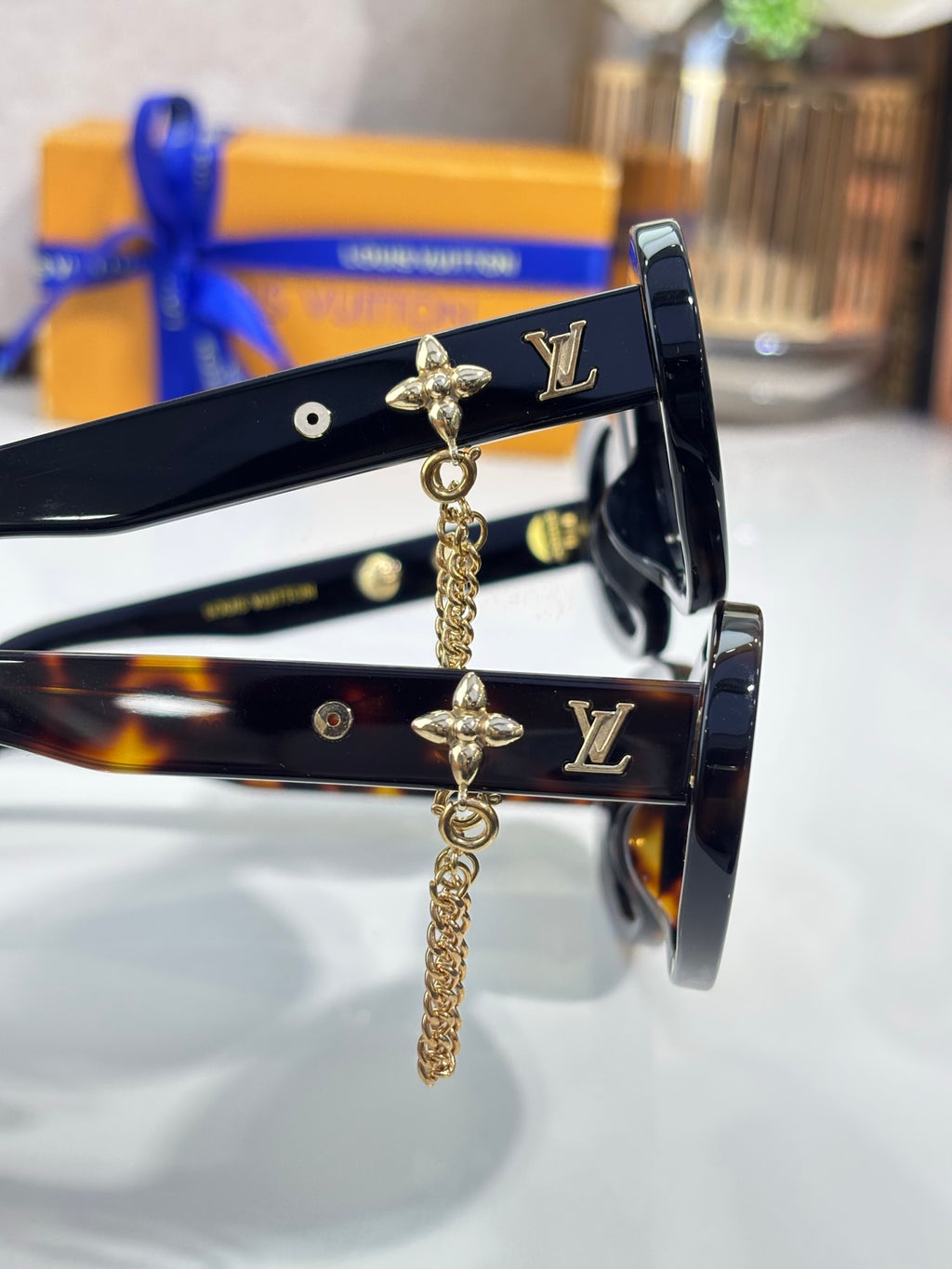 Louis Vuitton black sunglasses close-up with gold logo studs and dangling chain charm