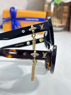 Louis Vuitton black sunglasses close-up with gold logo studs and dangling chain charm