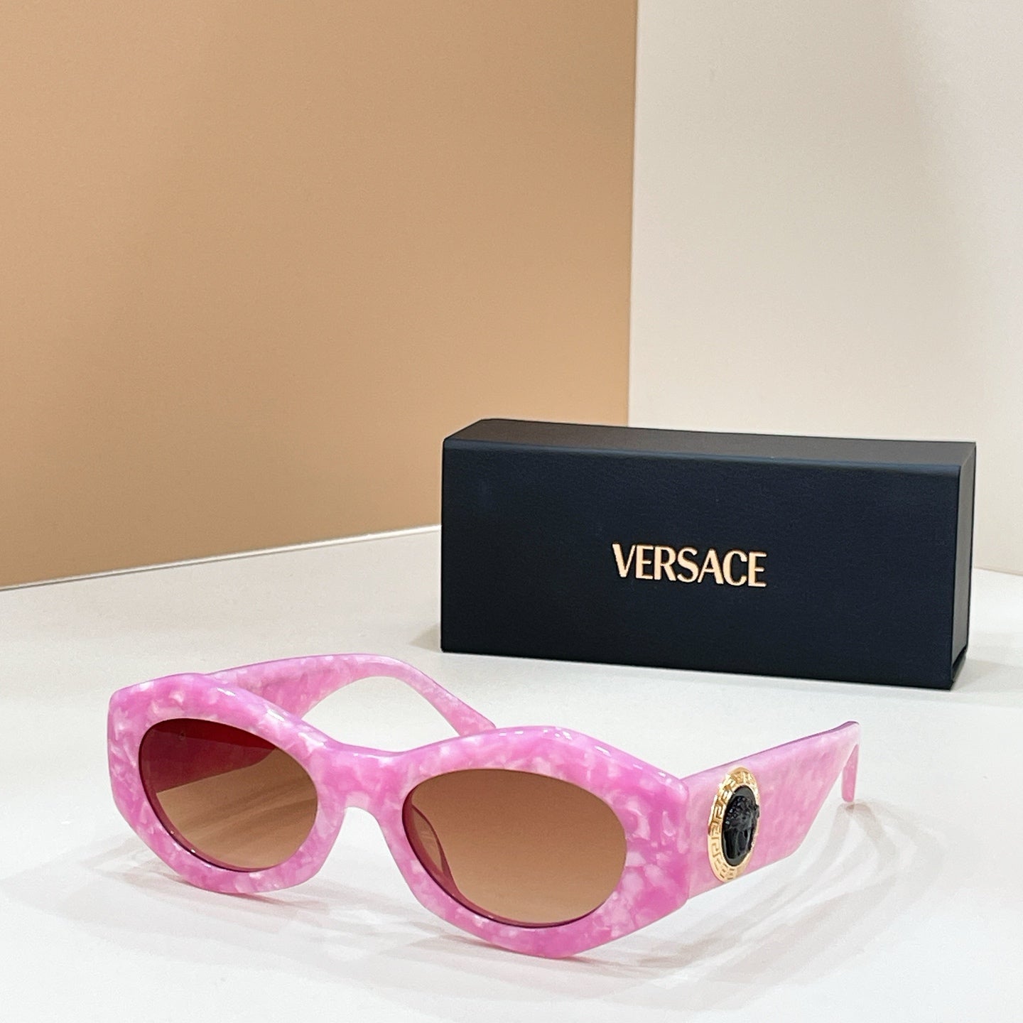 Pink cat-eye sunglasses with tinted lenses and gold logo medallion on the temple