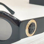 Close-up of black sunglasses frame with gold logo medallion at the temple