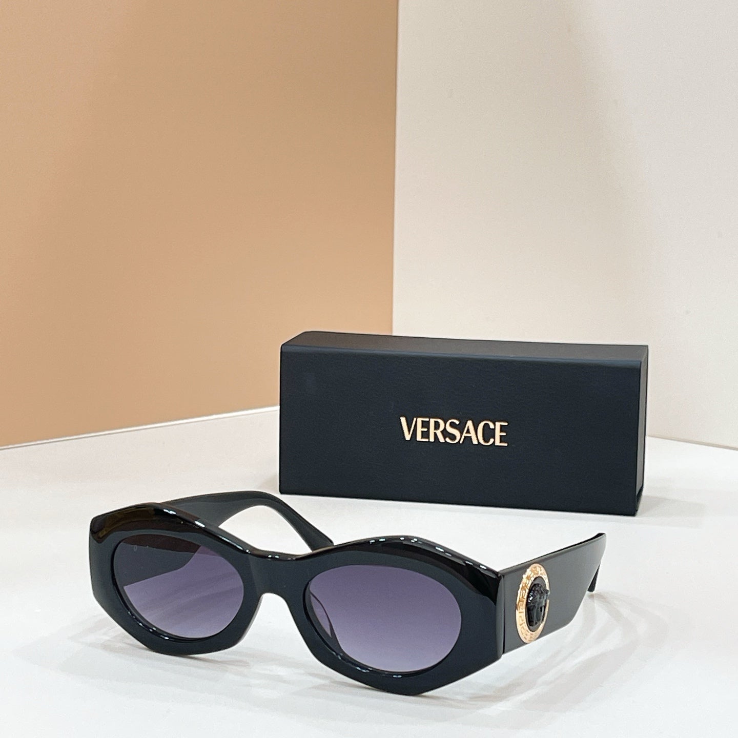 Black cat-eye sunglasses with purple-tinted lenses and gold logo medallion on the temple