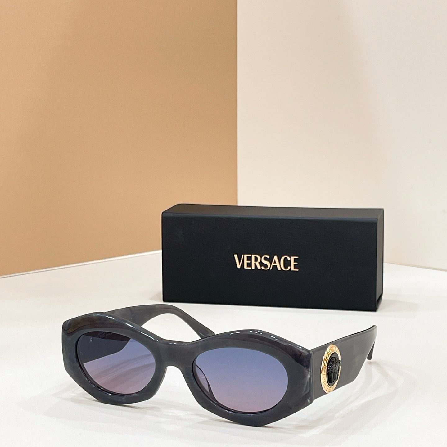 Dark sunglasses with purple-tinted lenses and gold logo medallion on the temple