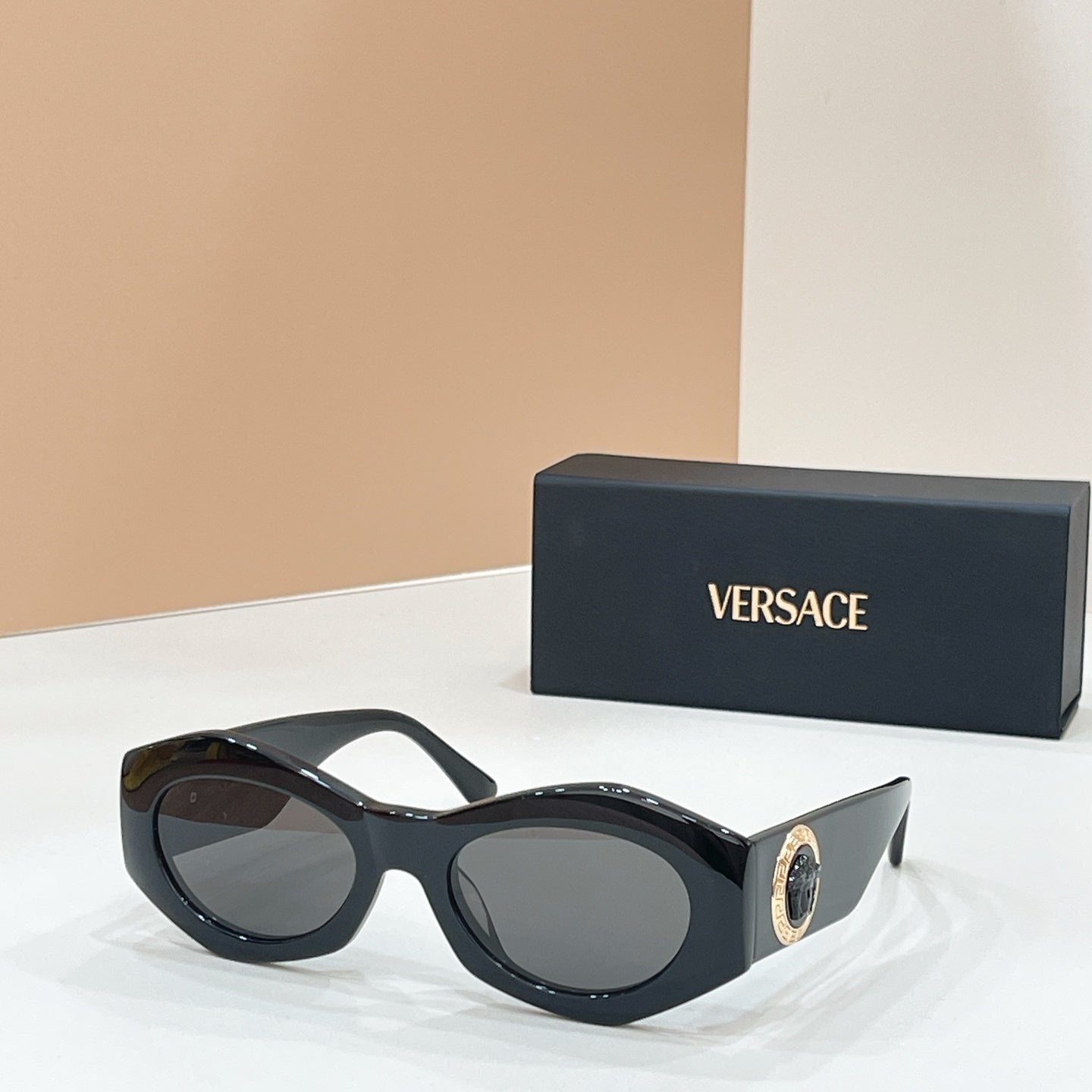 Black sunglasses with oval lenses and gold logo medallion on the temple