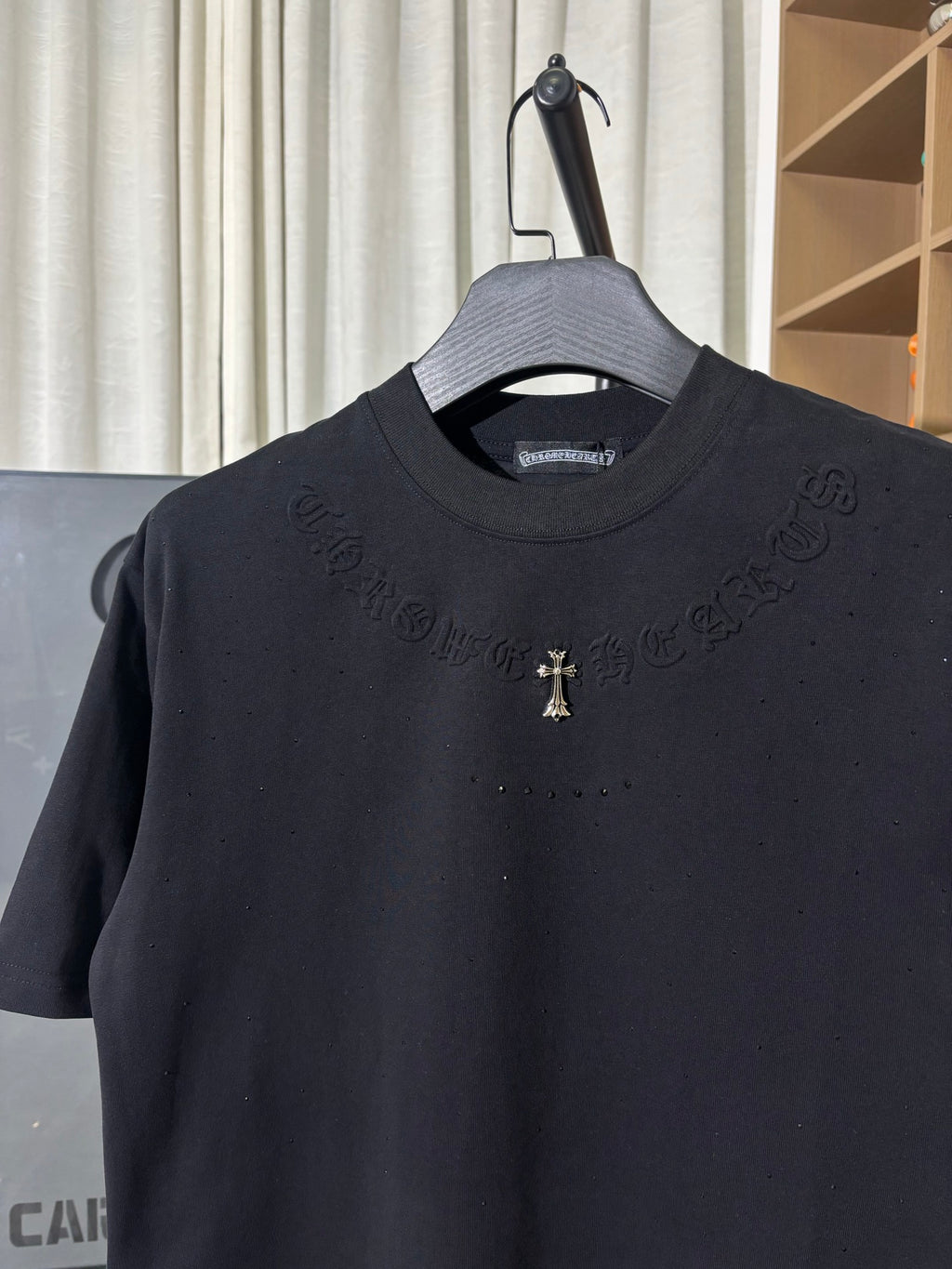 Black crew-neck T-shirt with subtle raised text pattern and small gold cross logo