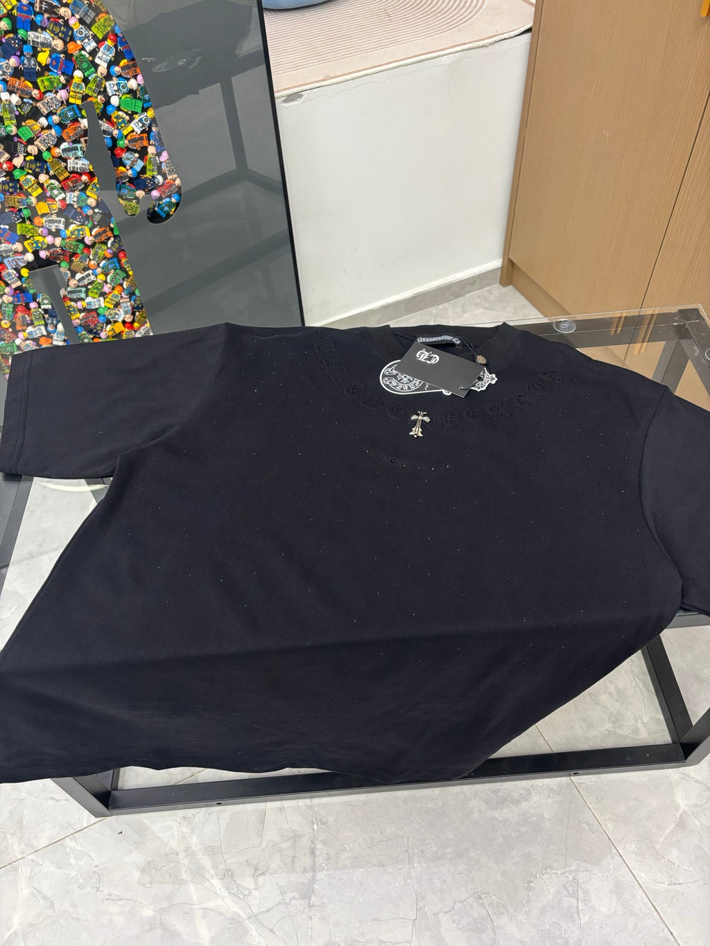Black crew-neck T-shirt lying flat, gold cross emblem and raised logo detail