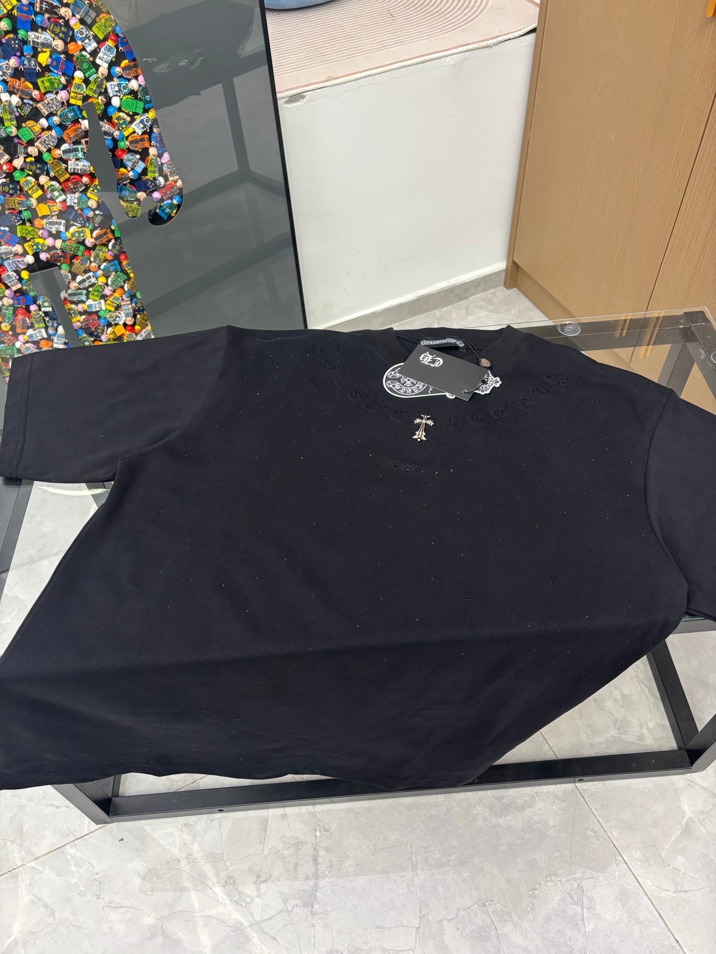 Black crew-neck T-shirt lying flat, gold cross emblem and raised logo detail