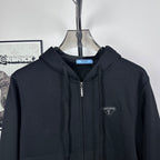 Dark zip-up hoodie close-up with hood, silver zipper, and small chest logo patch