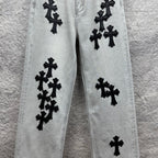 Light wash denim pants with scattered black cross appliqués along the legs