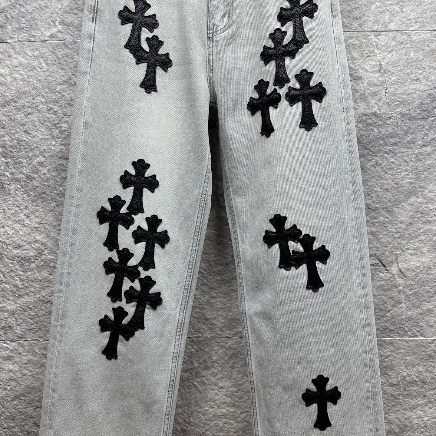 Light wash denim pants with scattered black cross appliqués along the legs
