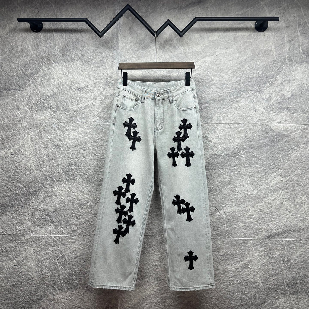Light wash denim pants with black cross appliqués, button fly, belt loops