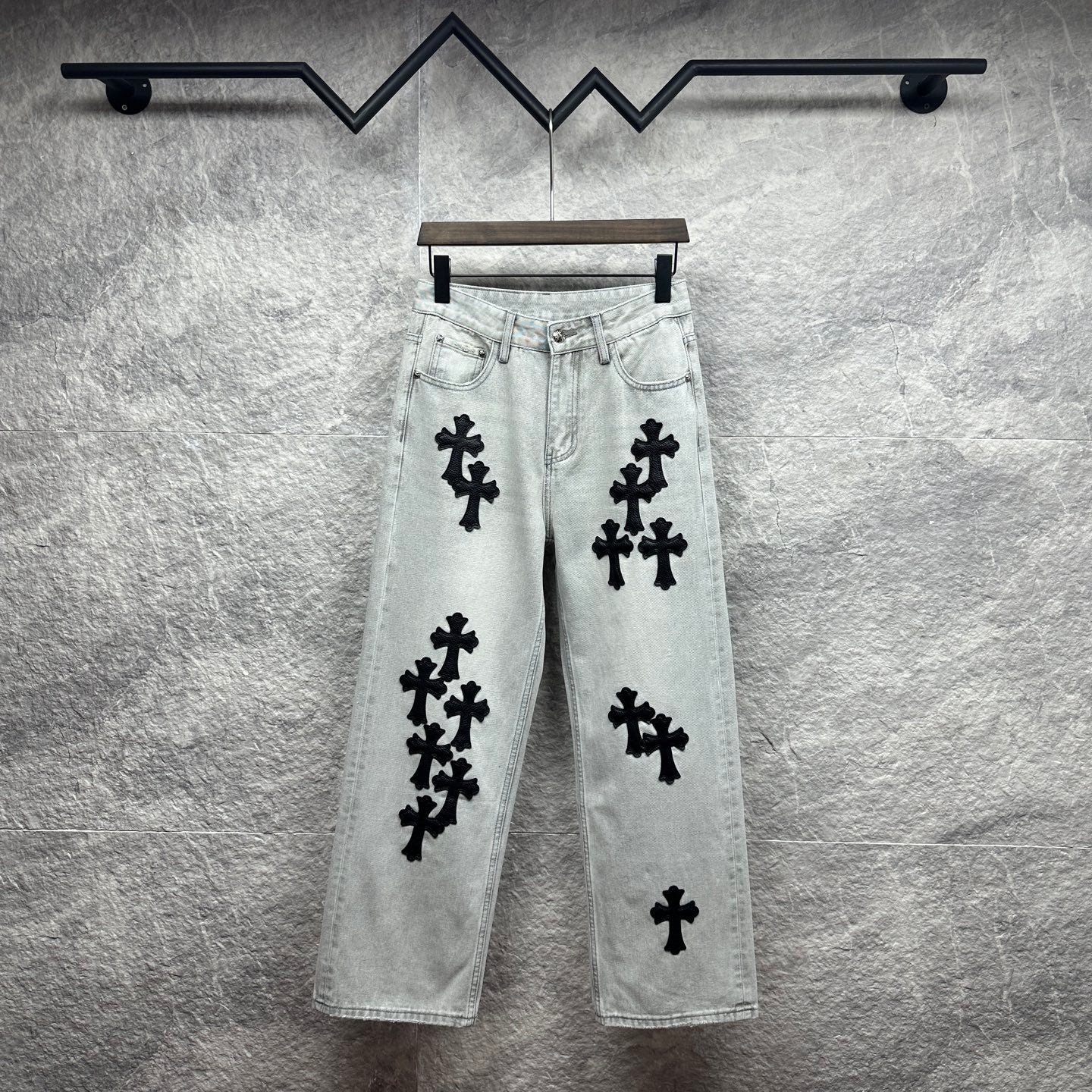 Light wash denim pants with black cross appliqués, button fly, belt loops