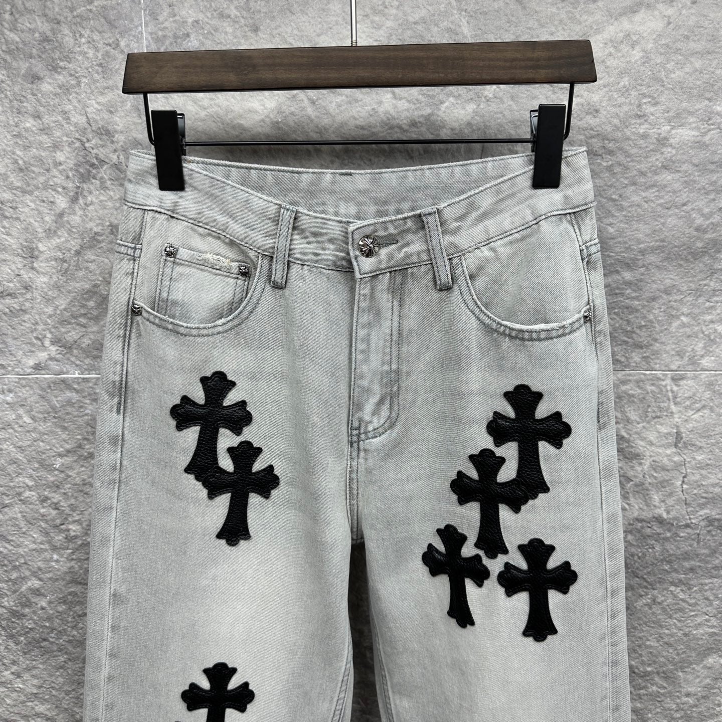 Light wash denim pants waistband with belt loops and black cross appliqués on front