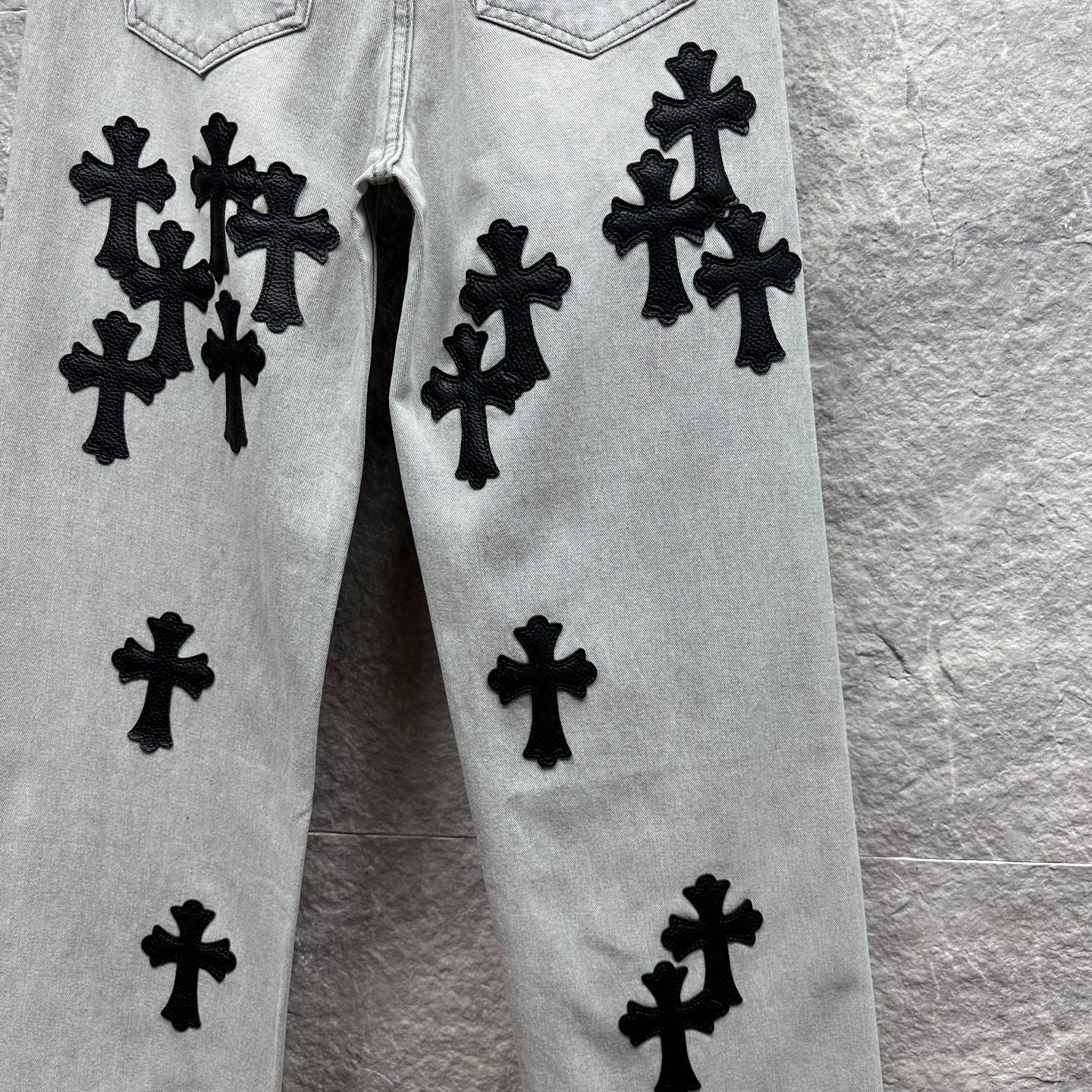 Light wash denim pants with black cross appliqués on front panels