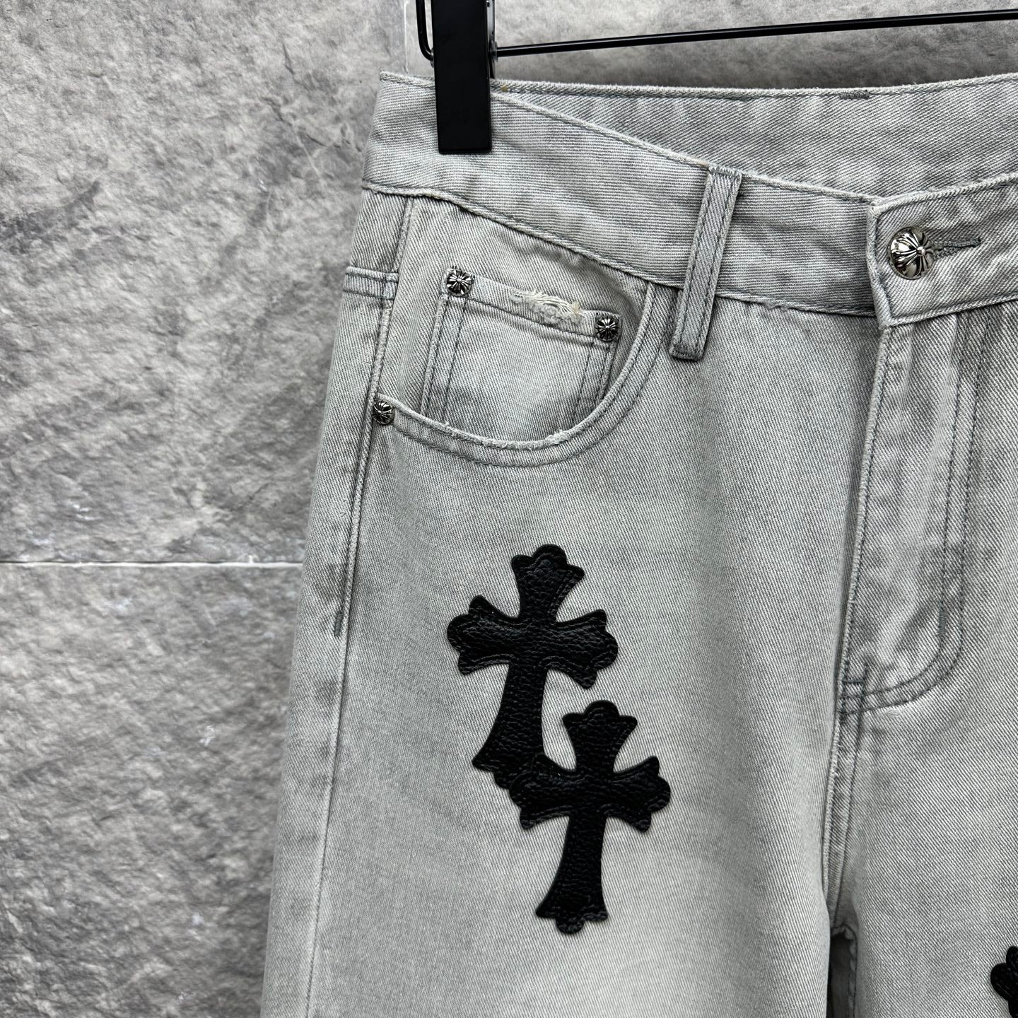 Light wash denim pants front pocket with black cross appliqué near hip