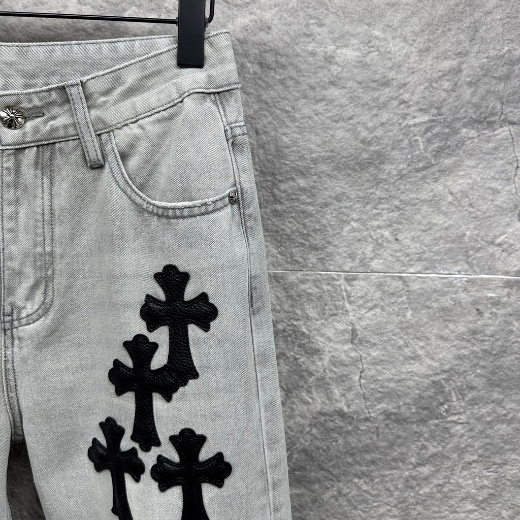 Light wash denim pants with black cross appliqués and curved front yoke