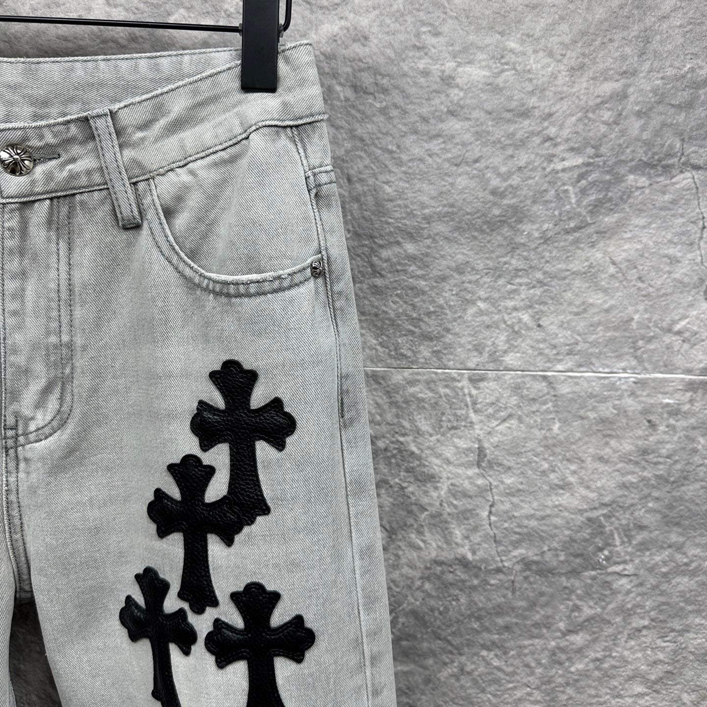 Light wash denim pants with black cross appliqués and curved front yoke