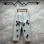 Light wash denim pants with black cross appliqués and tan leather patch at waistband