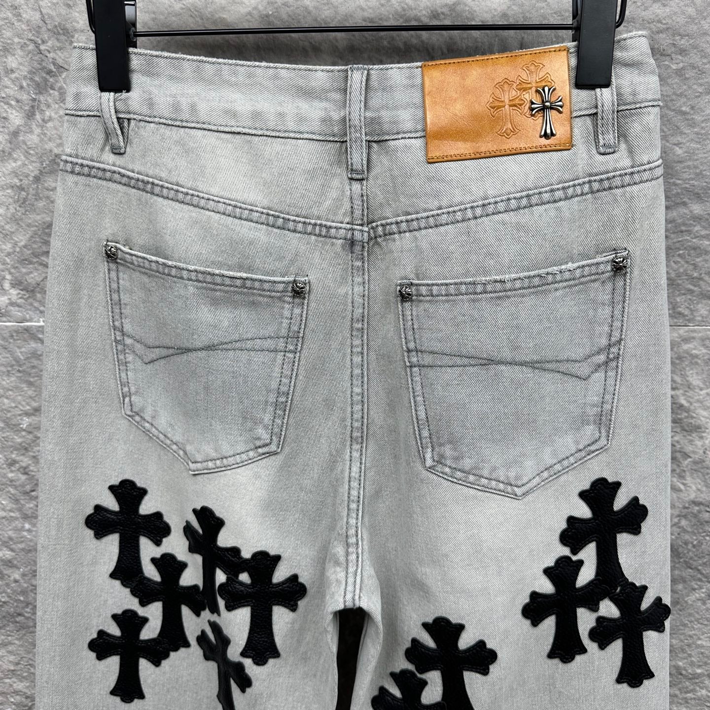Light wash denim pants with back pockets and black cross appliqués, tan waist patch