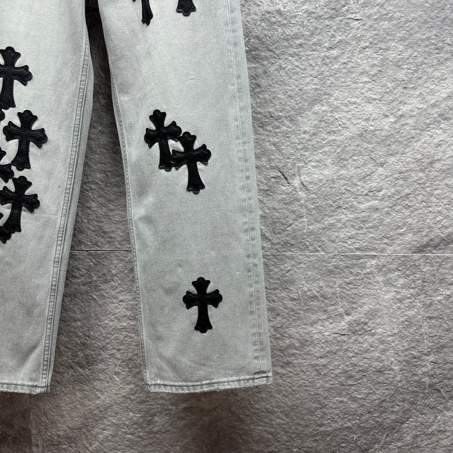 Light wash denim pants leg with scattered black cross appliqués