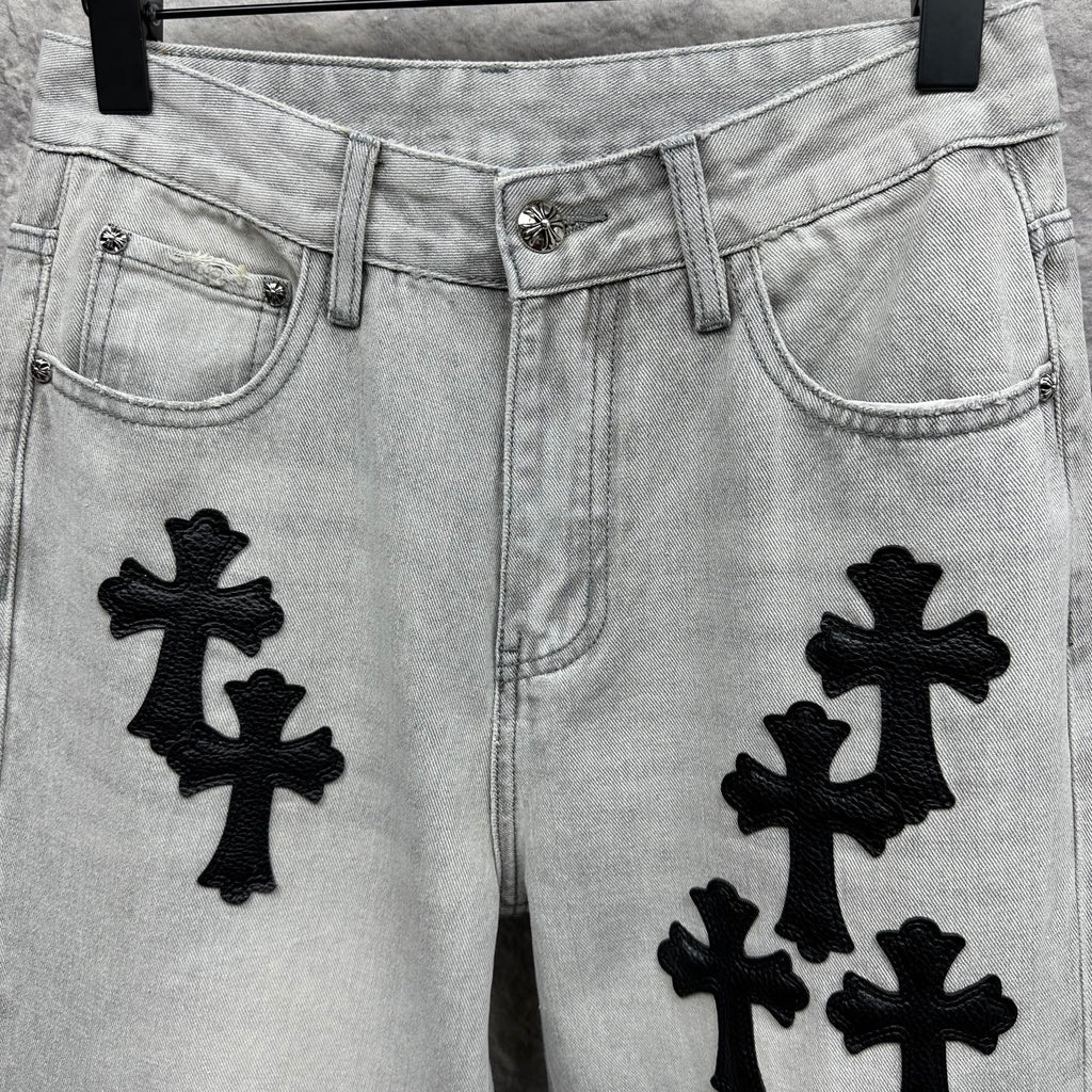 Light wash denim pants with black cross appliqués, front pockets and button closure
