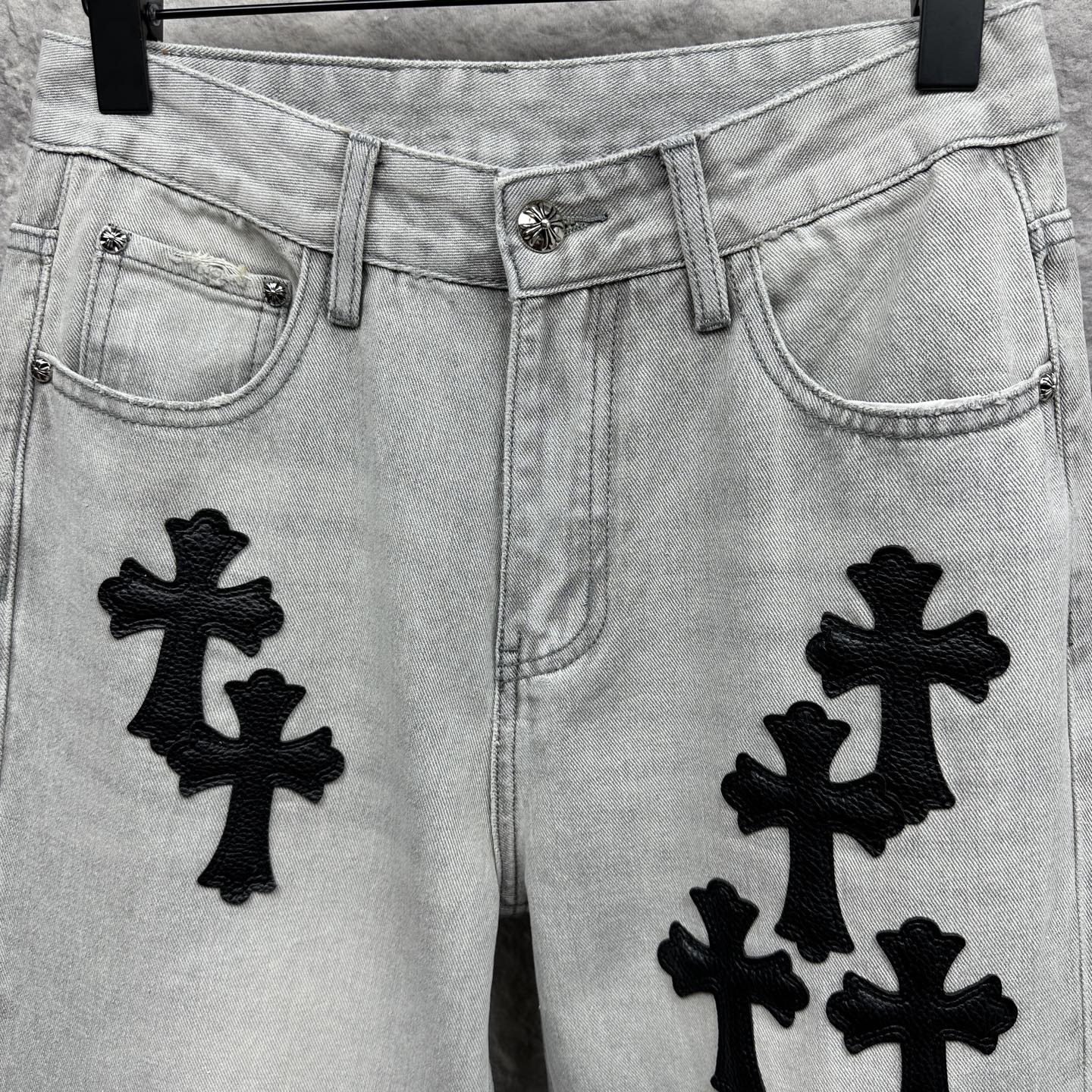 Light wash denim pants with black cross appliqués, front pockets and button closure