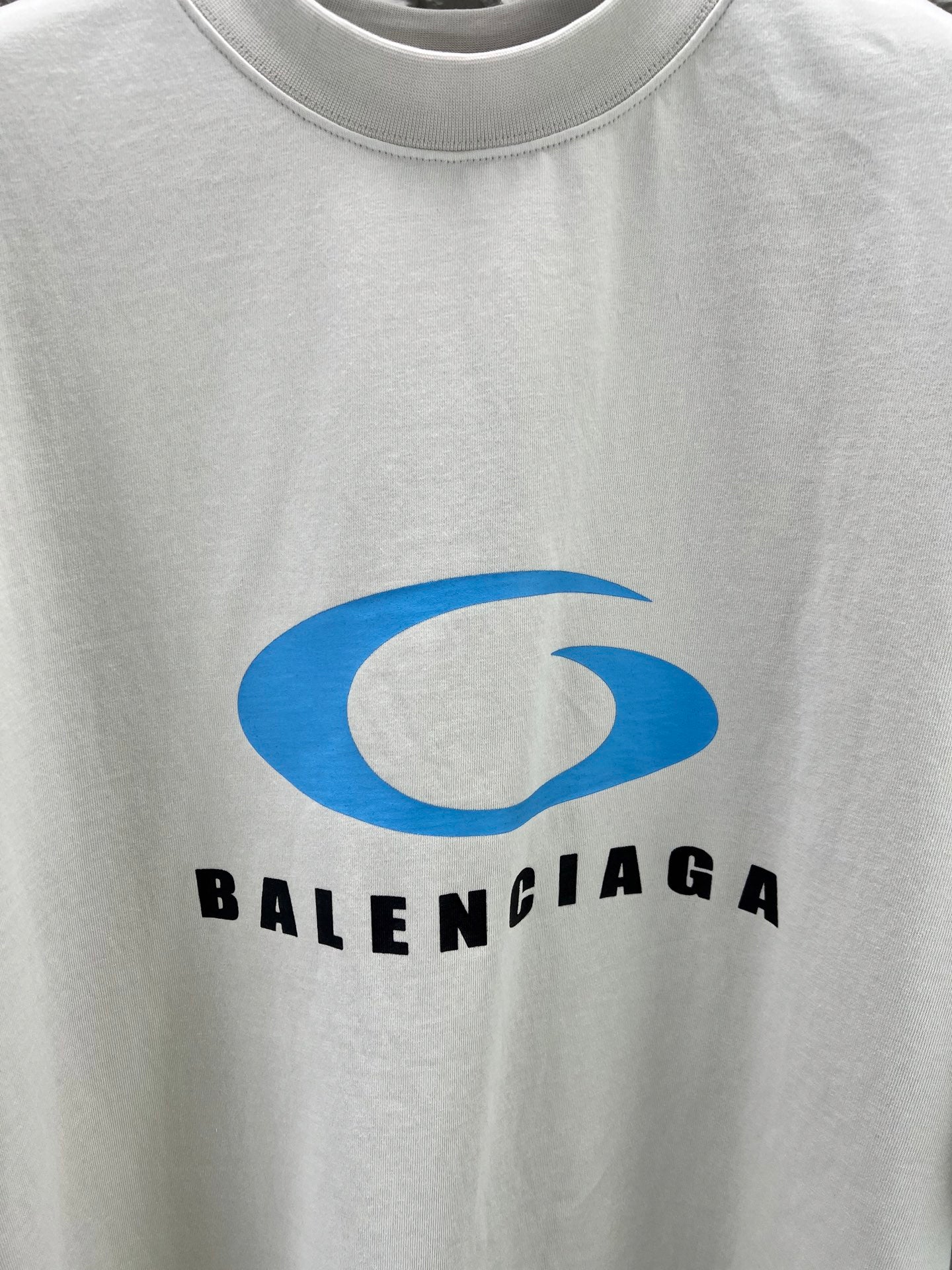 Close-up of white T-shirt chest graphic: blue Balenciaga logo and text