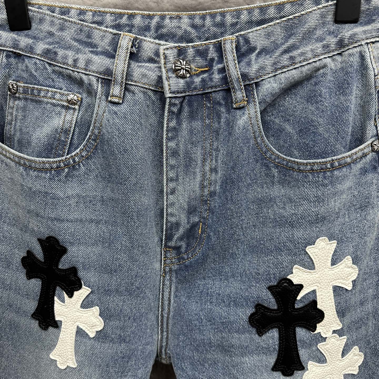 Light blue denim pants close-up: waistband, pockets, and cross applique on both legs