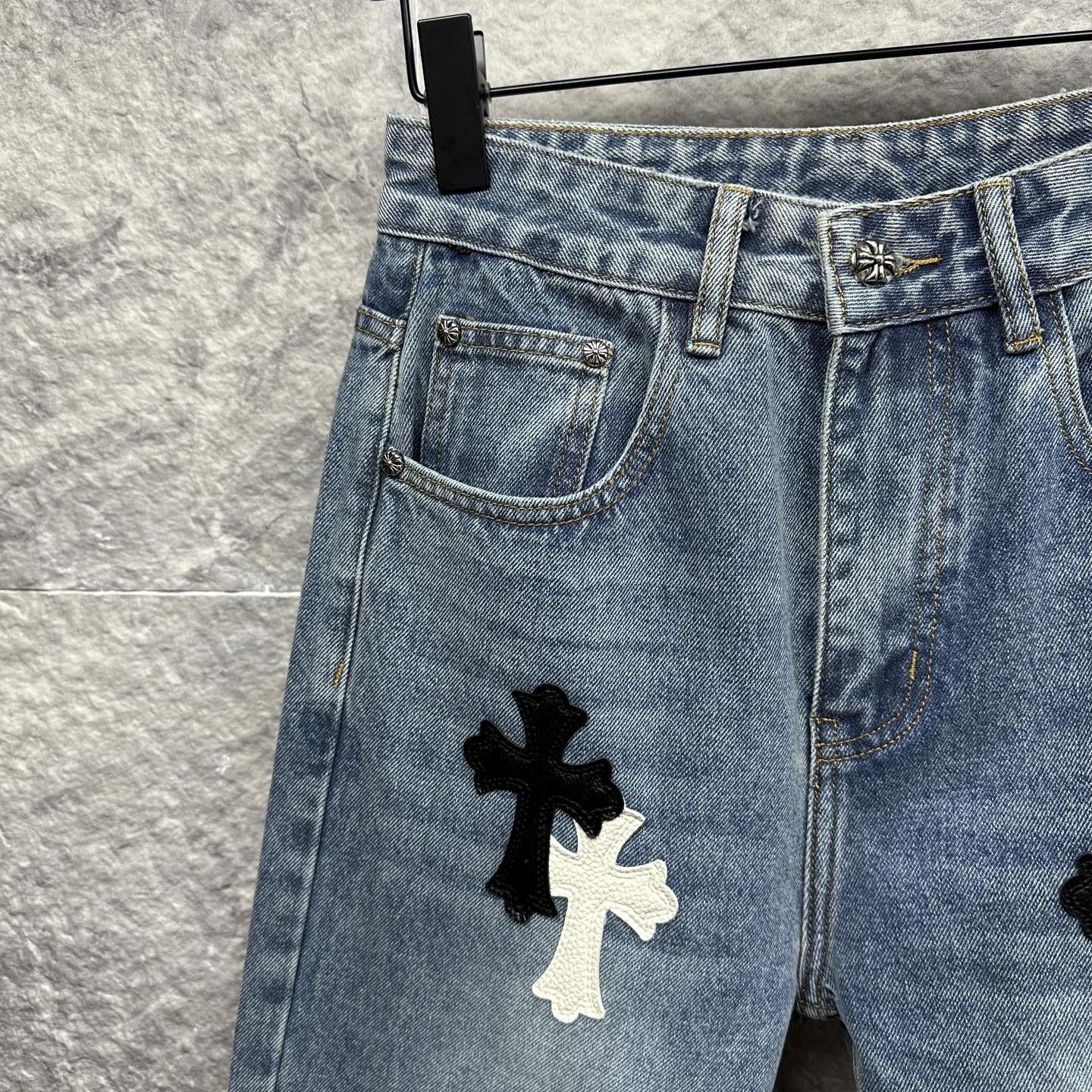 Light blue denim pants close-up of front pocket and thigh with cross applique