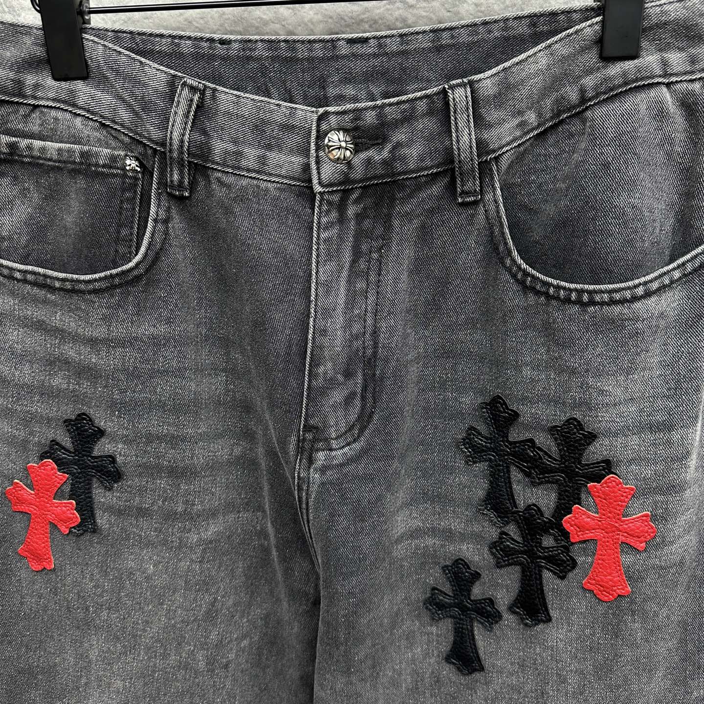 Grey denim pants with waistband detail, side pockets, and cross embroidery