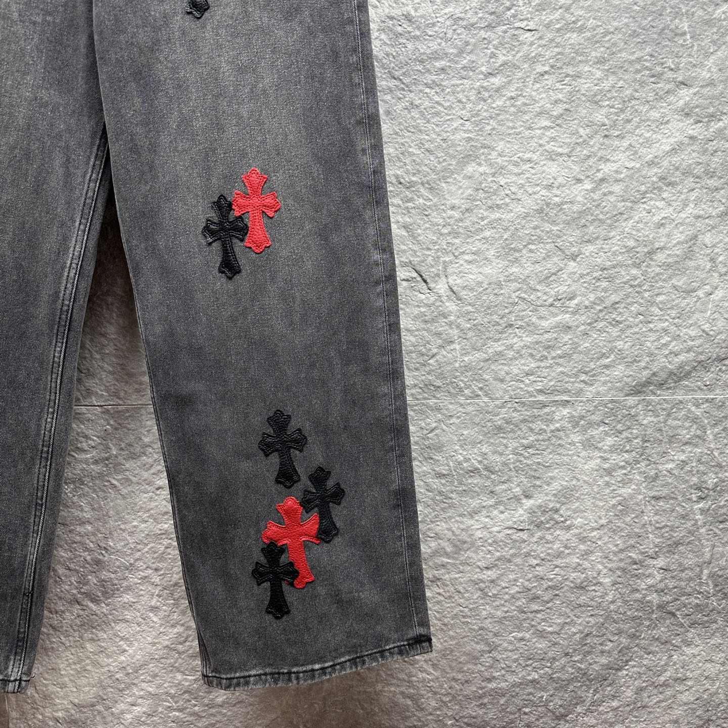 Grey denim pants with red and black cross embroidery on lower leg