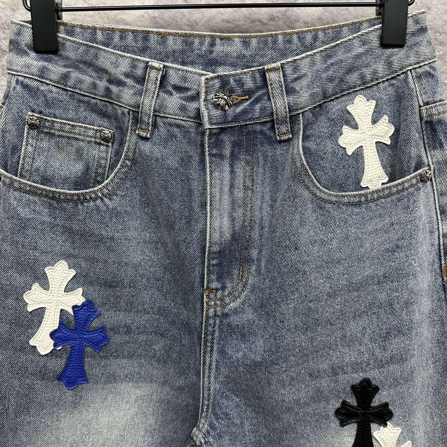 Light-wash denim pants with cross patches on the front and pockets, button waistband