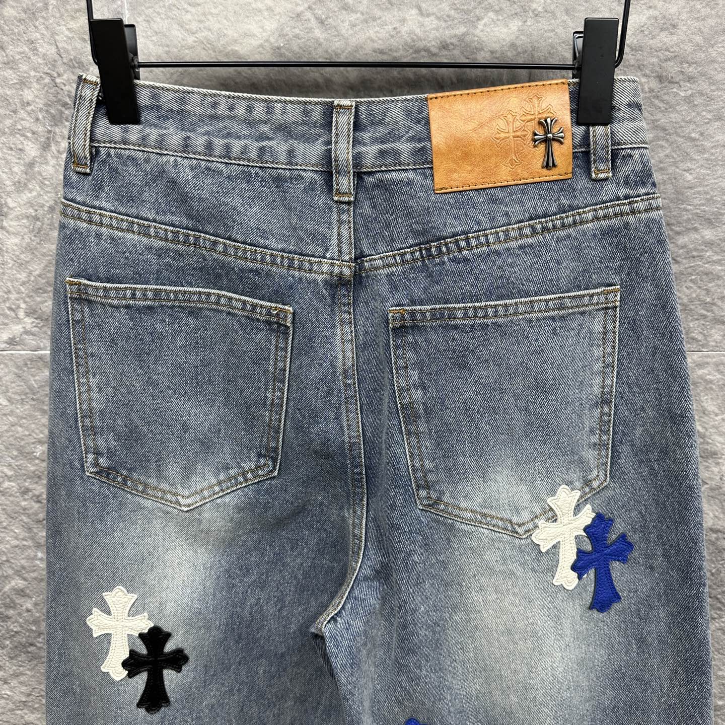Light-wash denim pants with cross patches and tan logo patch at waistband