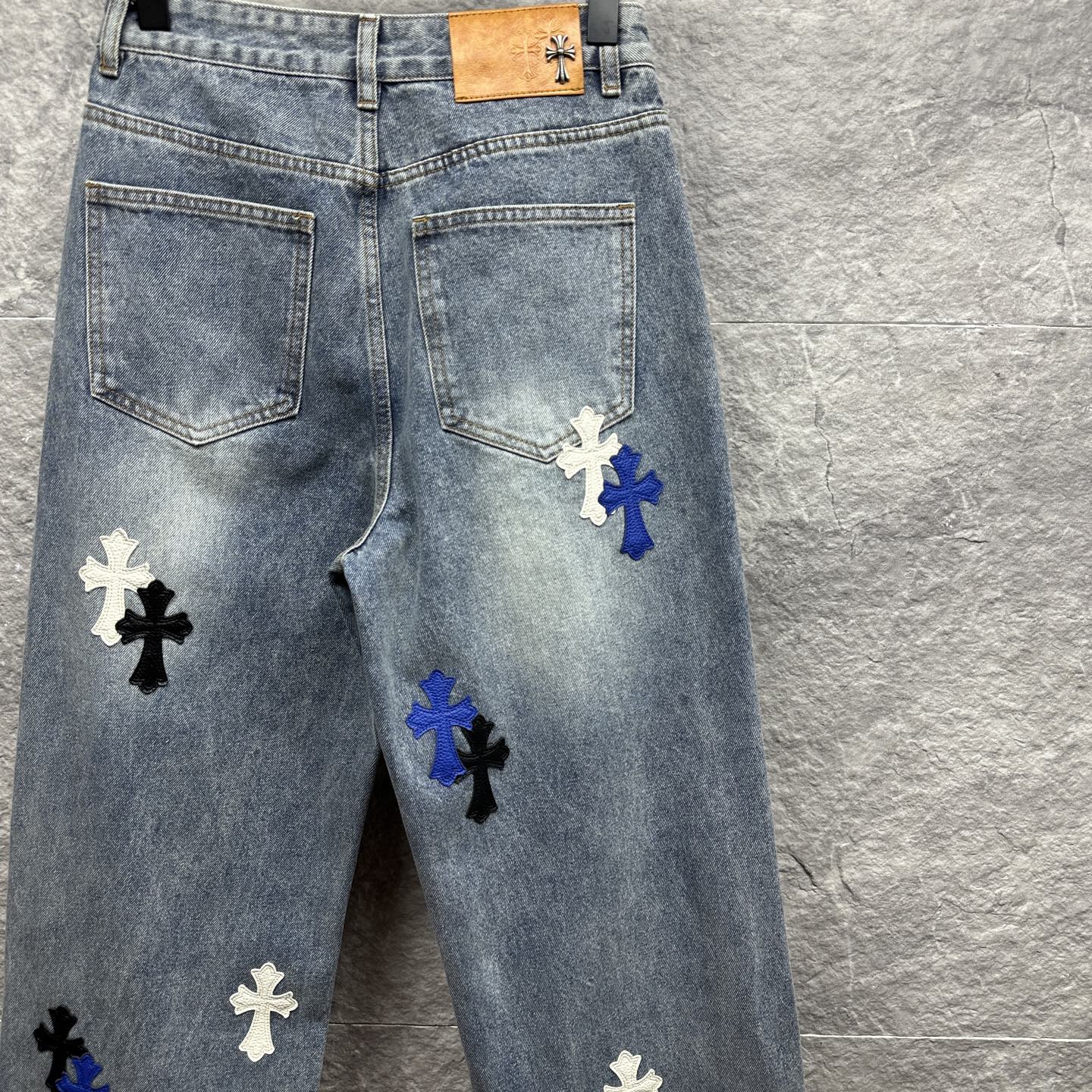 Light-wash denim pants with cross patches on the front legs and tan waistband label