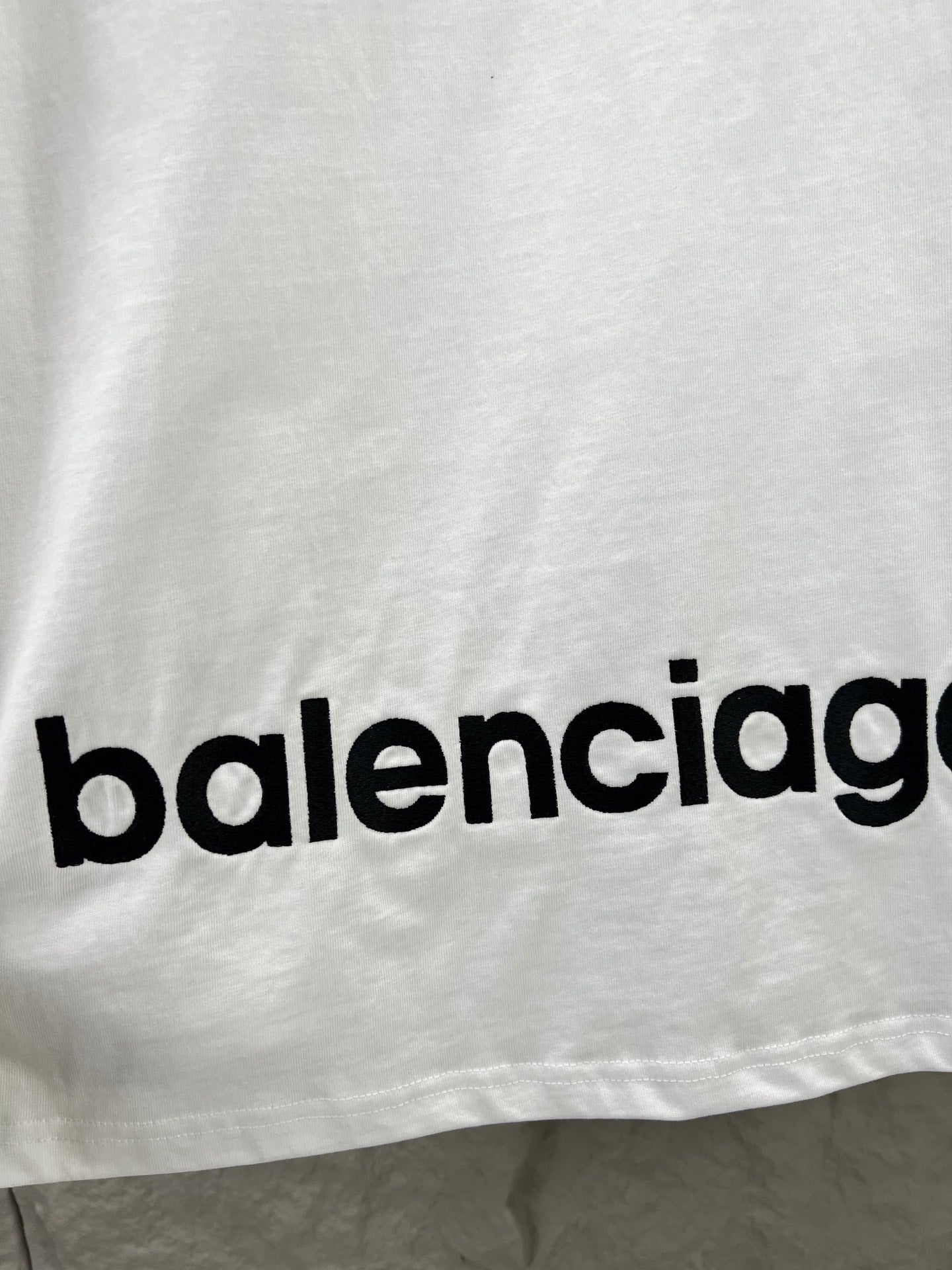 Close-up of “balenciag…” text logo on the hem of a white T-shirt.