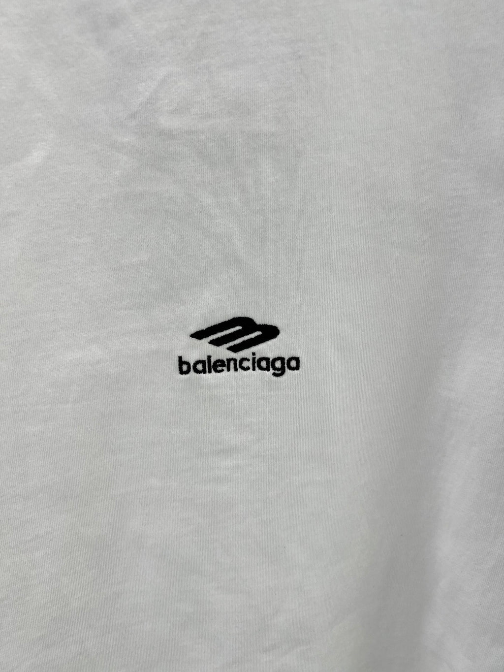 Close-up of white T-shirt fabric with small black Balenciaga logo.