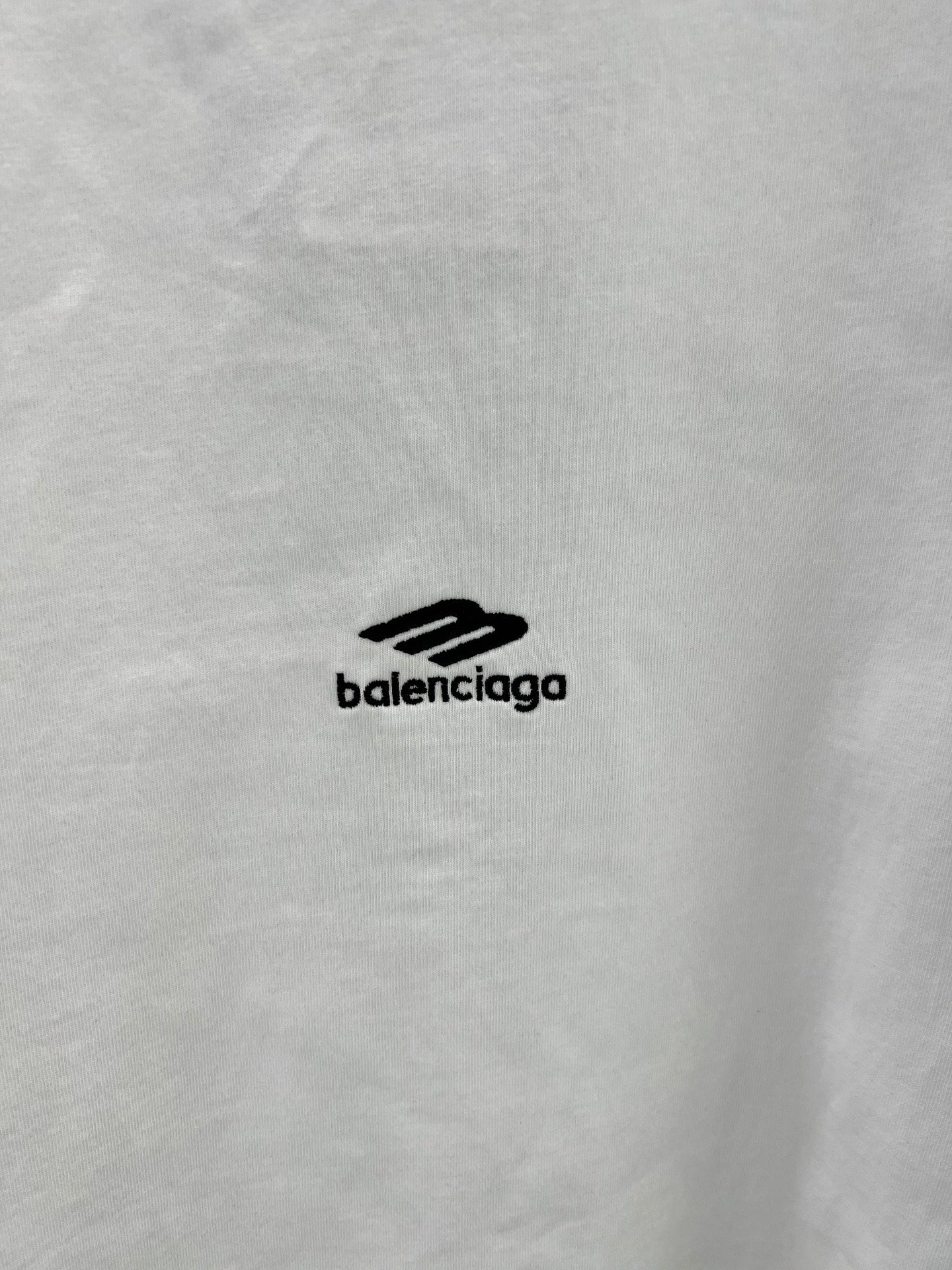 Close-up of white T-shirt fabric with small black Balenciaga logo.