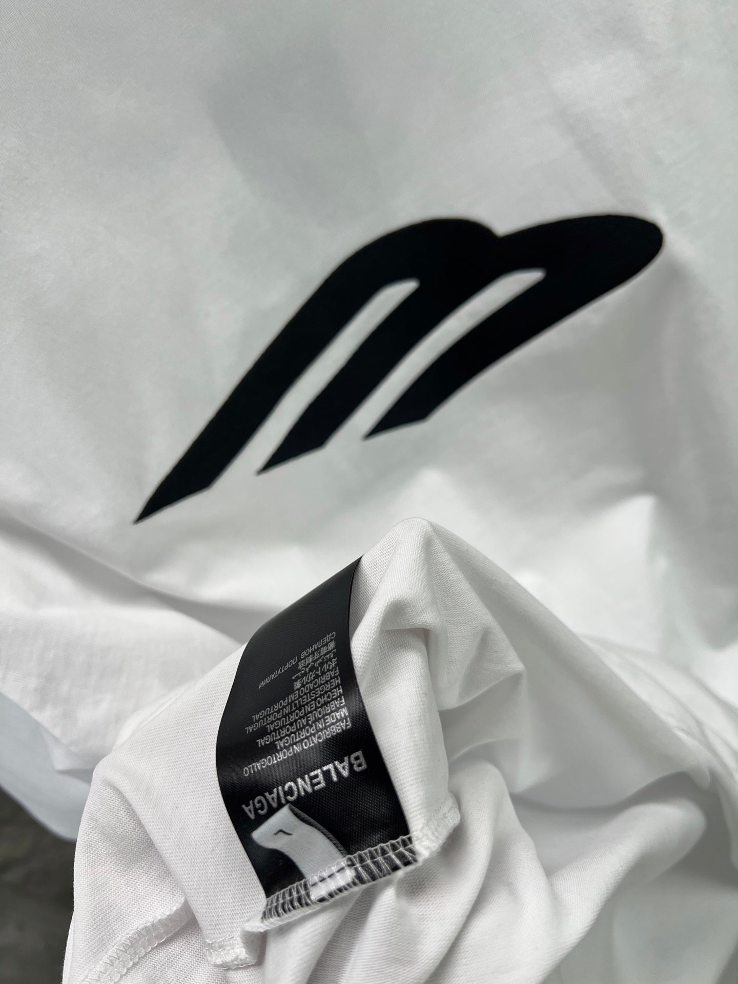 White crew-neck T-shirt with large black logo and woven neck label.
