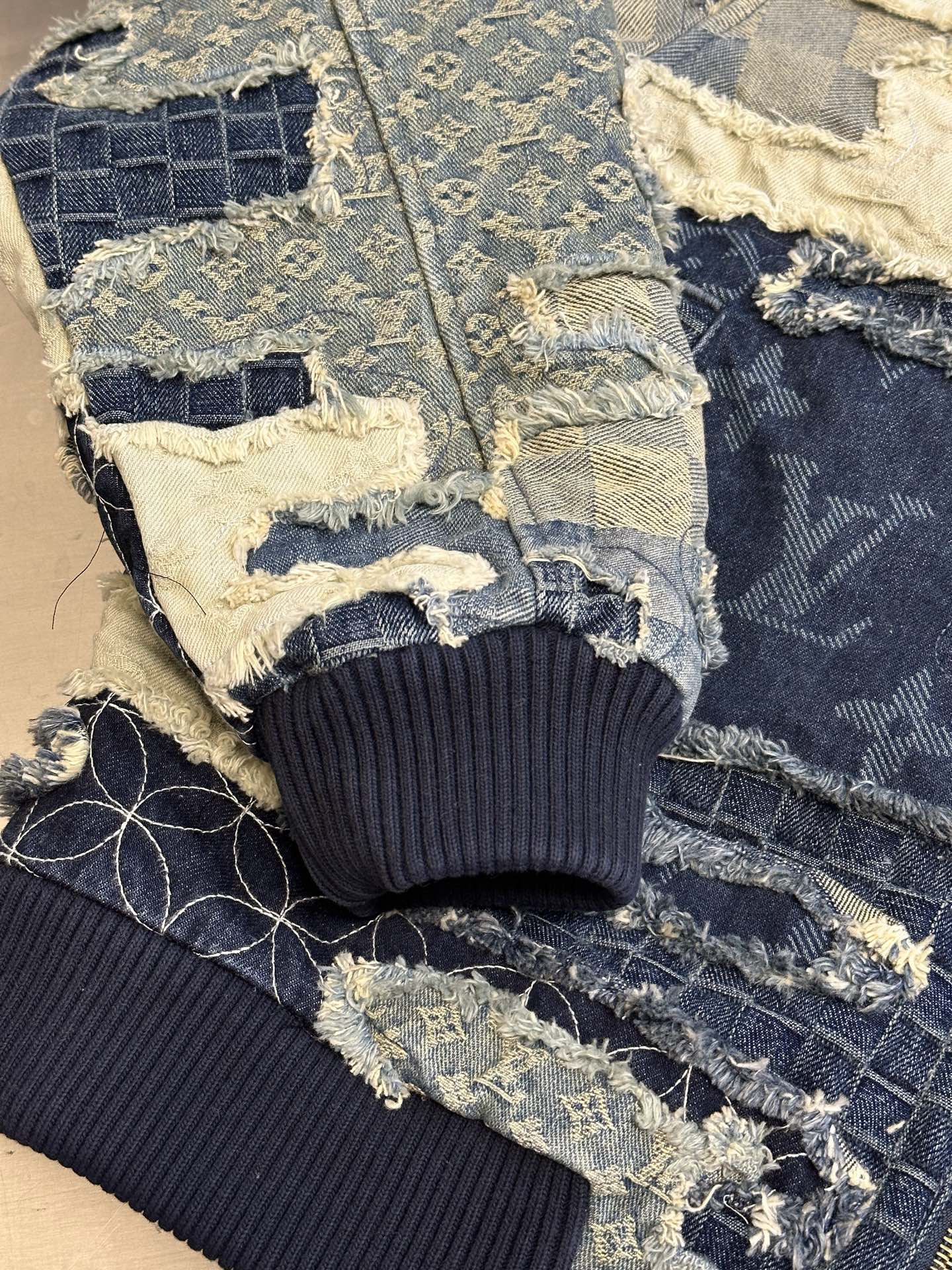 Denim jacket close-up showing ribbed cuffs and patchwork panels with blue-and-cream stitching