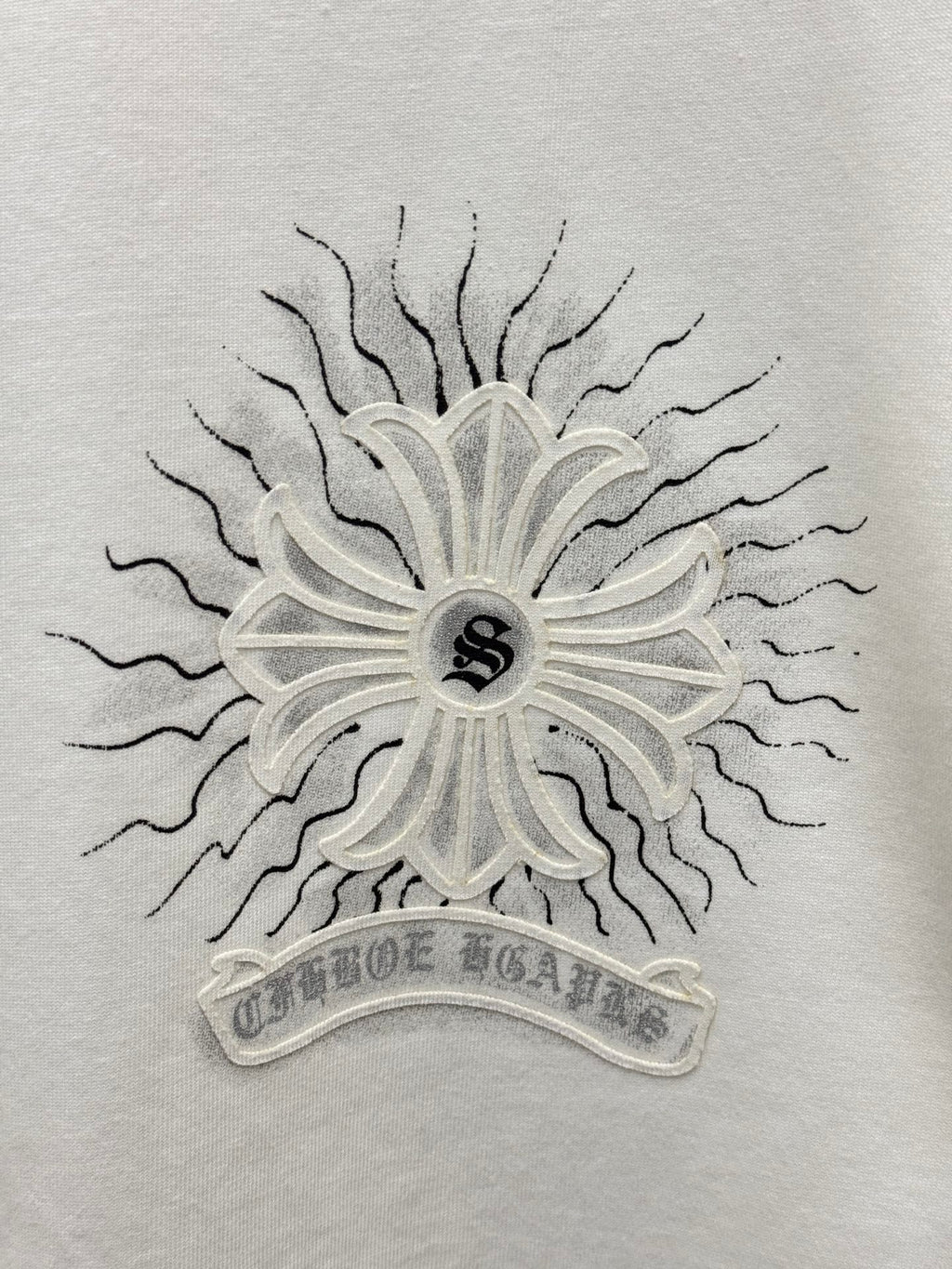 White T-shirt close-up of central sunburst floral emblem with small dark center