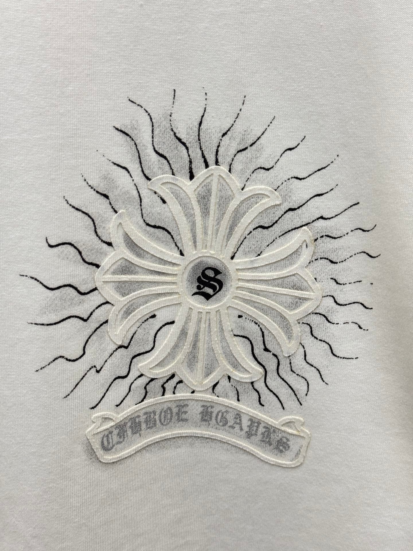 White T-shirt close-up of central sunburst floral emblem with small dark center