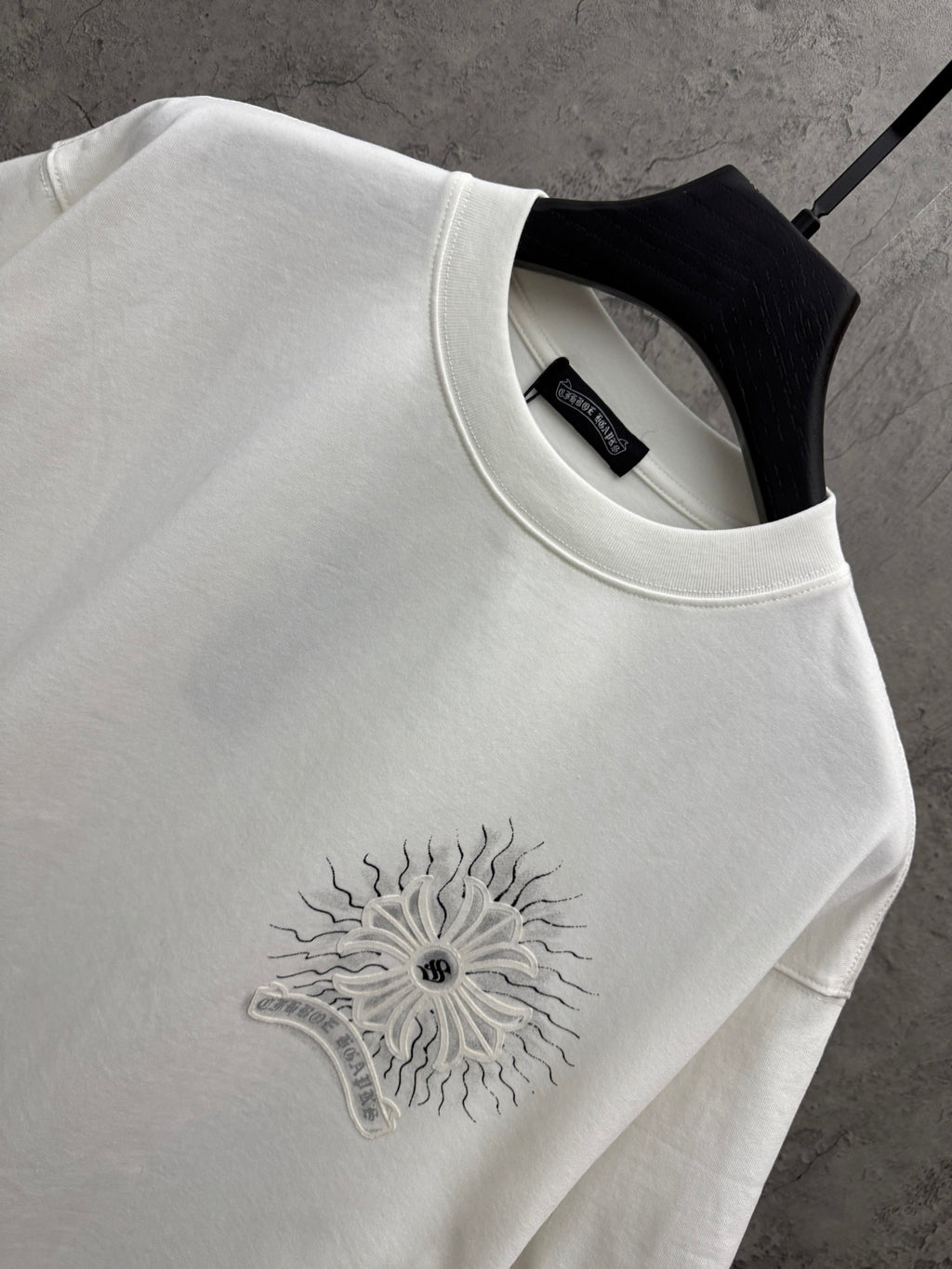 White short-sleeve T-shirt neckline detail with embroidered-style sunburst floral logo