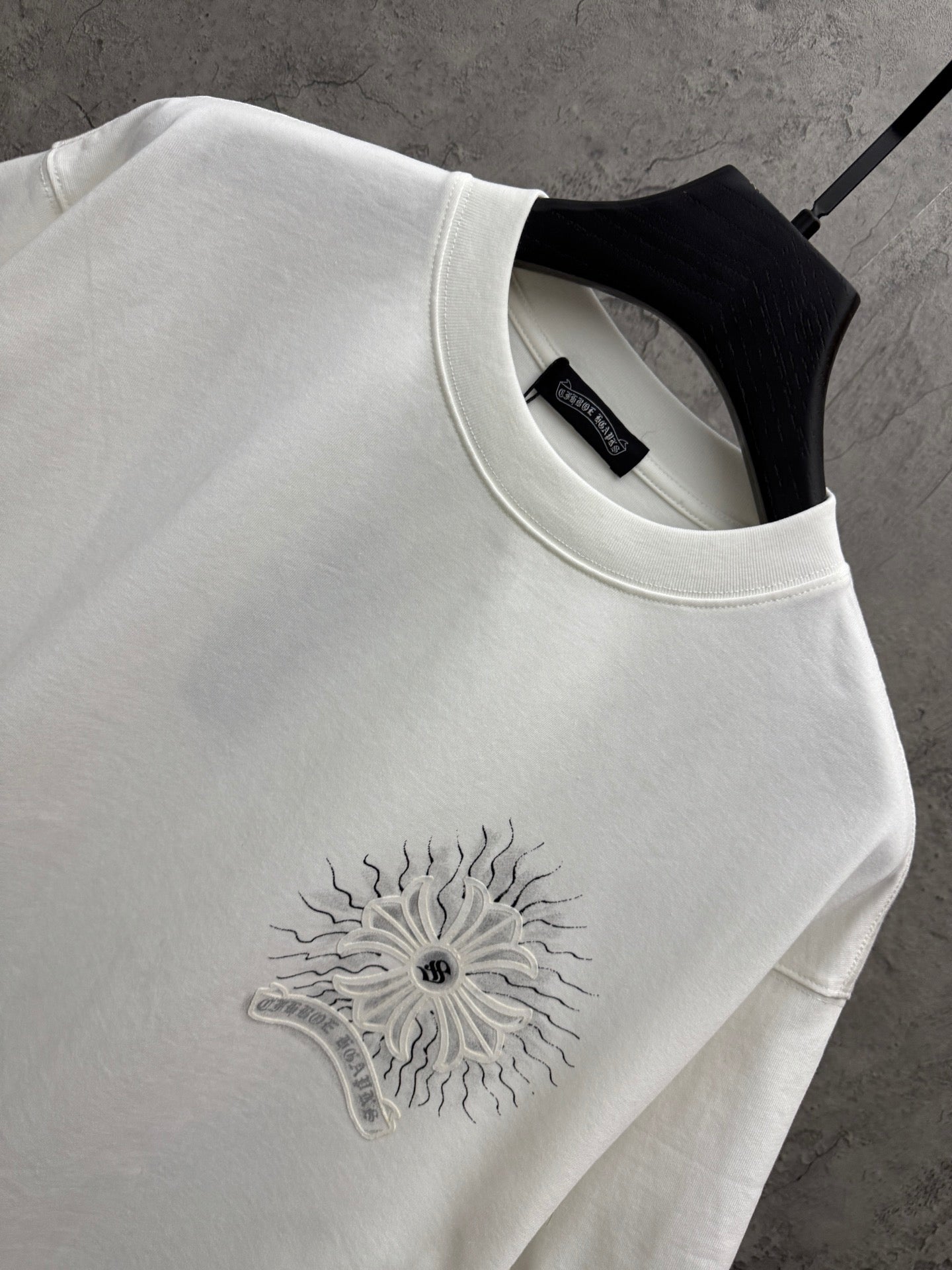 White short-sleeve T-shirt neckline detail with embroidered-style sunburst floral logo